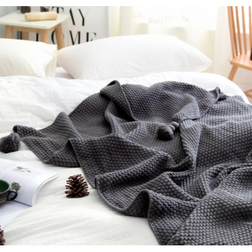 Grovstrikket vaffelpledd med pomponger til sofaen